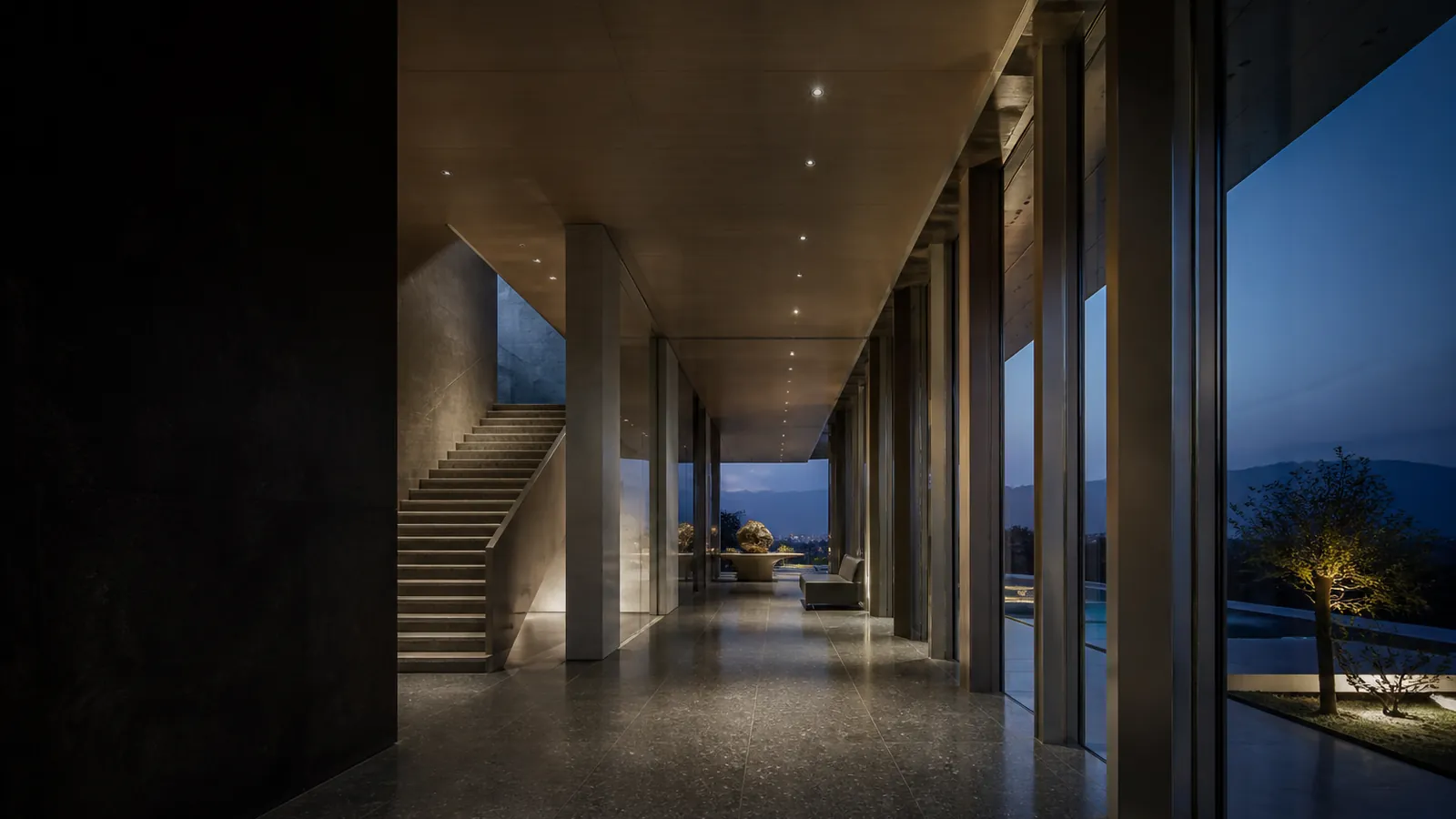 A refined architectural gallery with stone, glass and a sculptural staircase at dusk.